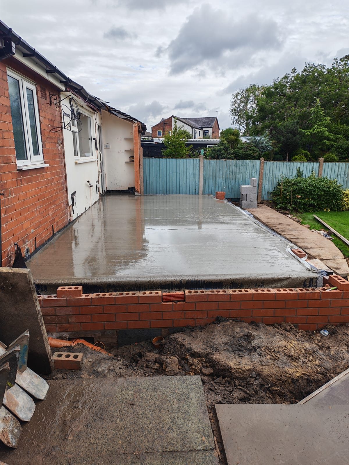 Newly poured concrete floor slab on a brick base running along the back of a bungalow